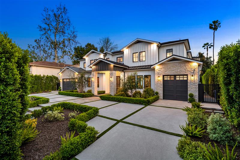 A modern two-story house in the evening with a large driveway and manicured landscaping.
